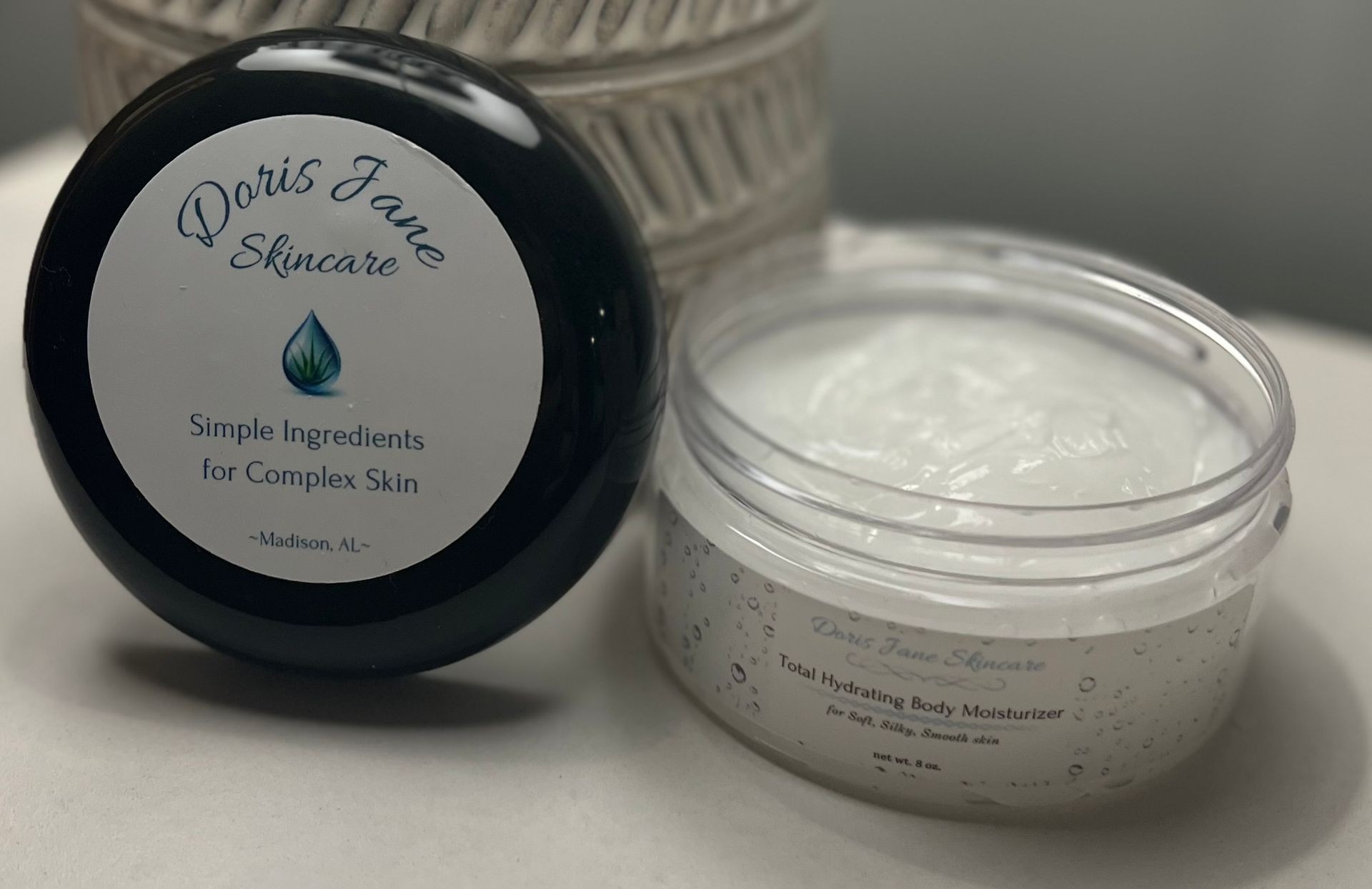 Two containers of Doris Jane Skincare, one closed and one open showing the body moisturizer inside.